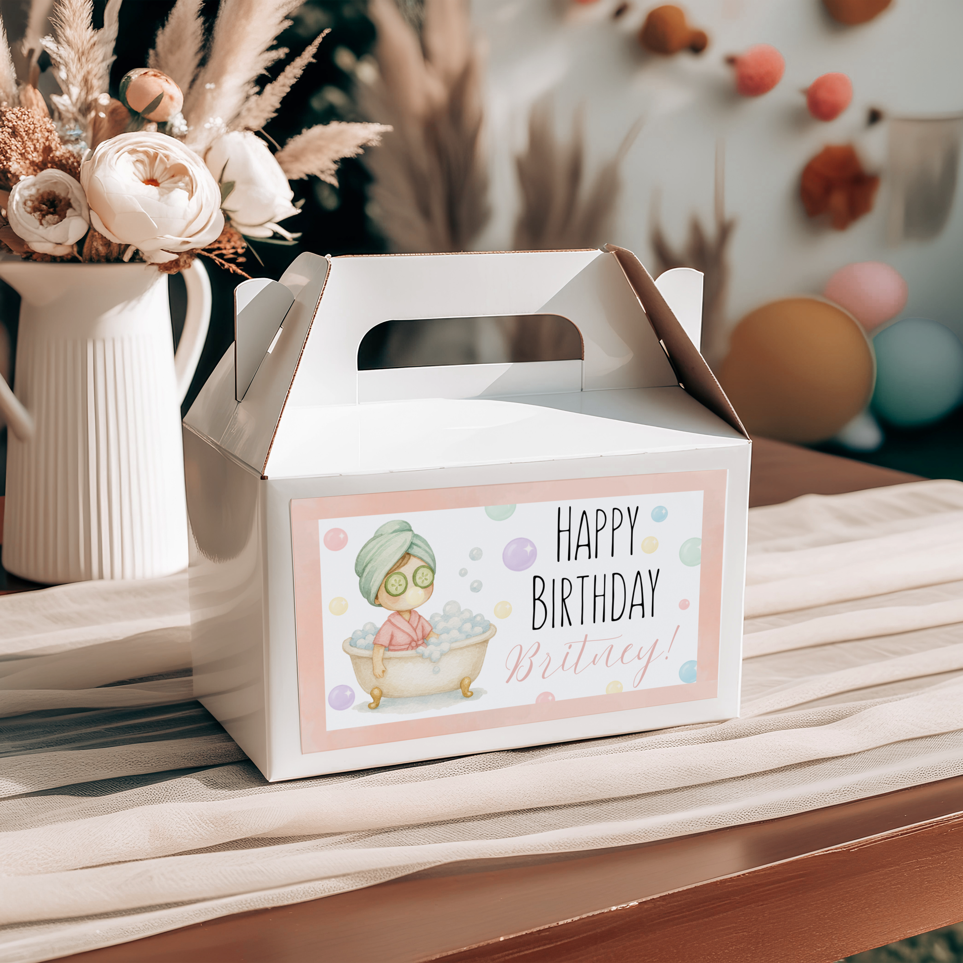 Gift box with a birthday card featuring a cartoon character on a wooden surface with flowers and balloons in the background.