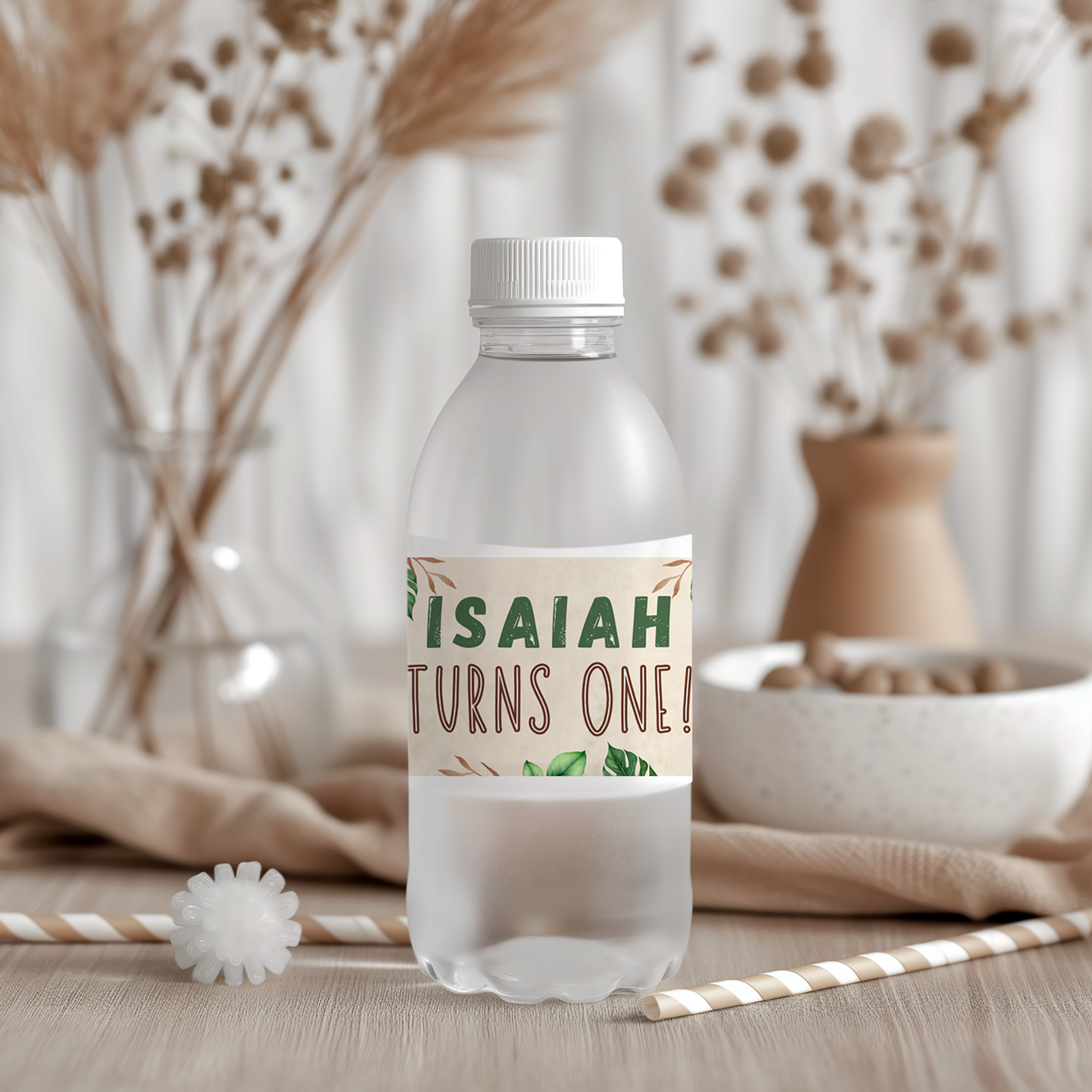 Clear water bottle with a personalized label reading 'ISAIAH TURNS ONE!' on a wooden surface with decorative elements.