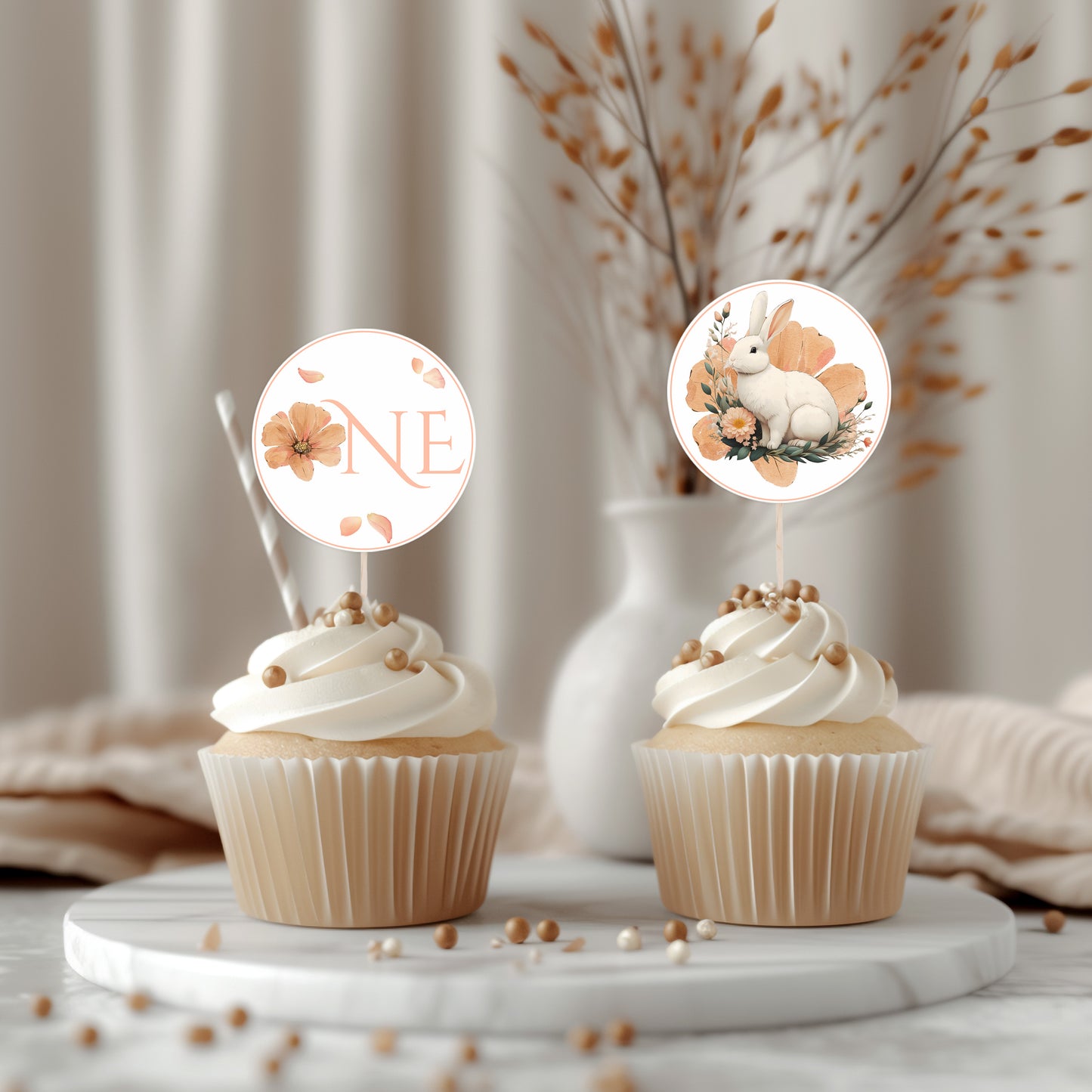 Two cupcakes with decorative toppers featuring a rabbit and floral design on a marble surface.