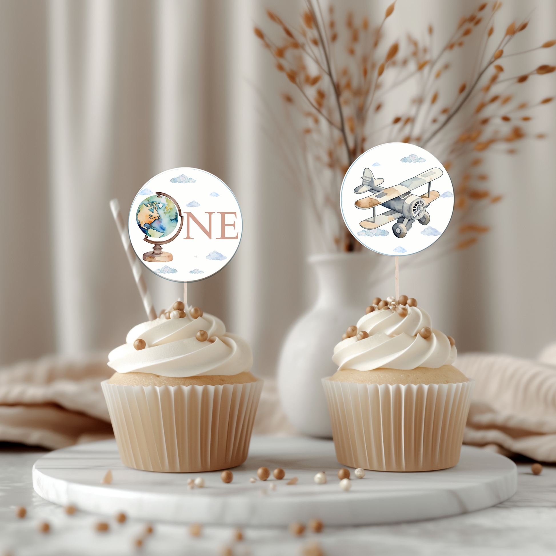 Two cupcakes with airplane and globe-themed toppers on a marble surface.