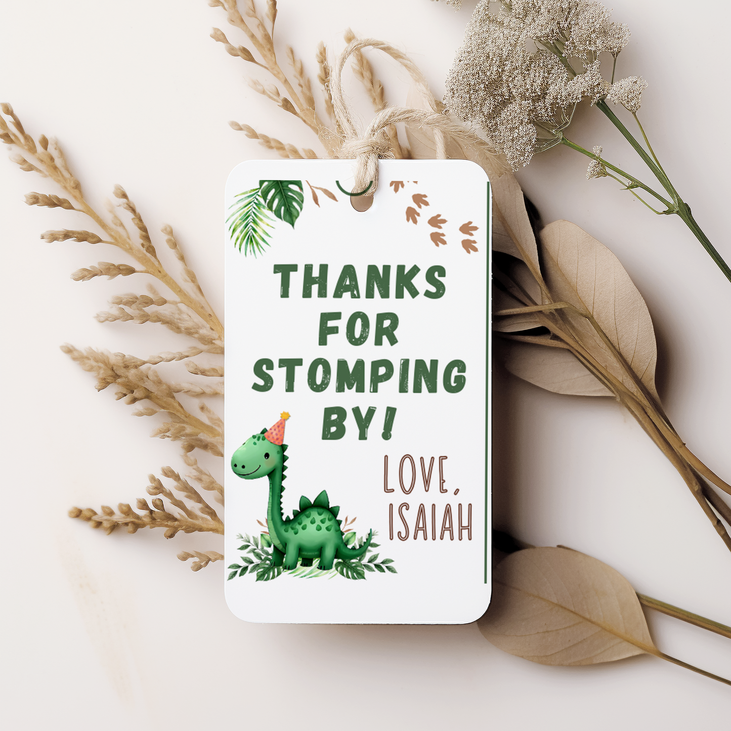 Gift tag with a dinosaur illustration and text 'Thanks for stomping by! Love, Isaiah' on a white background with dried plants.