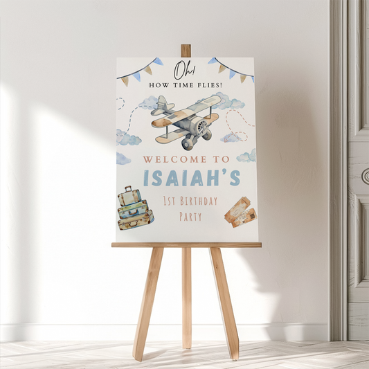 Birthday party sign with airplane and suitcase illustrations on a wooden easel.