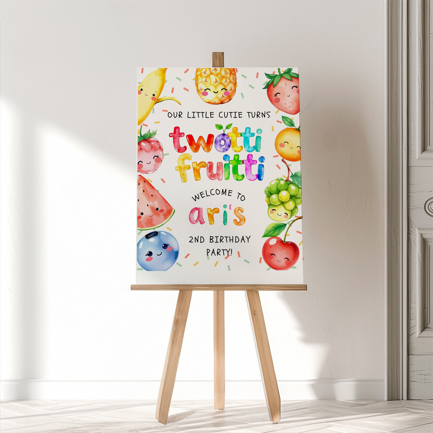 Birthday party invitation with fruit illustrations on a stand against a white wall.