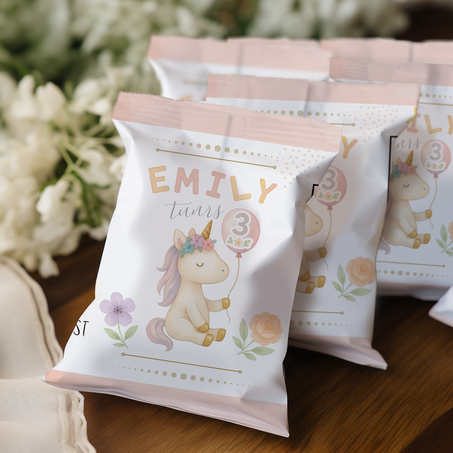 Party favor bags with unicorn design and text 'EMILY turns 3' on a wooden surface.