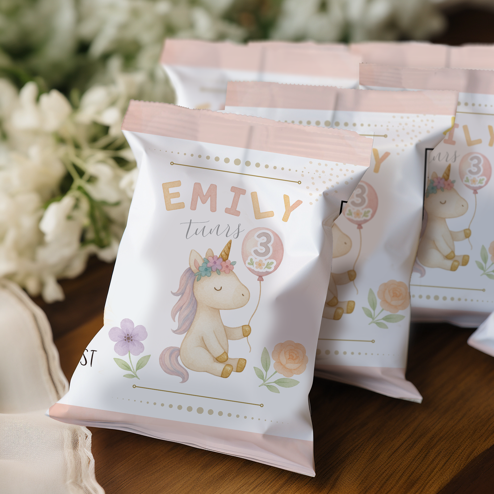 Party favor bags with unicorn design and text 'EMILY turns 3' on a wooden surface.