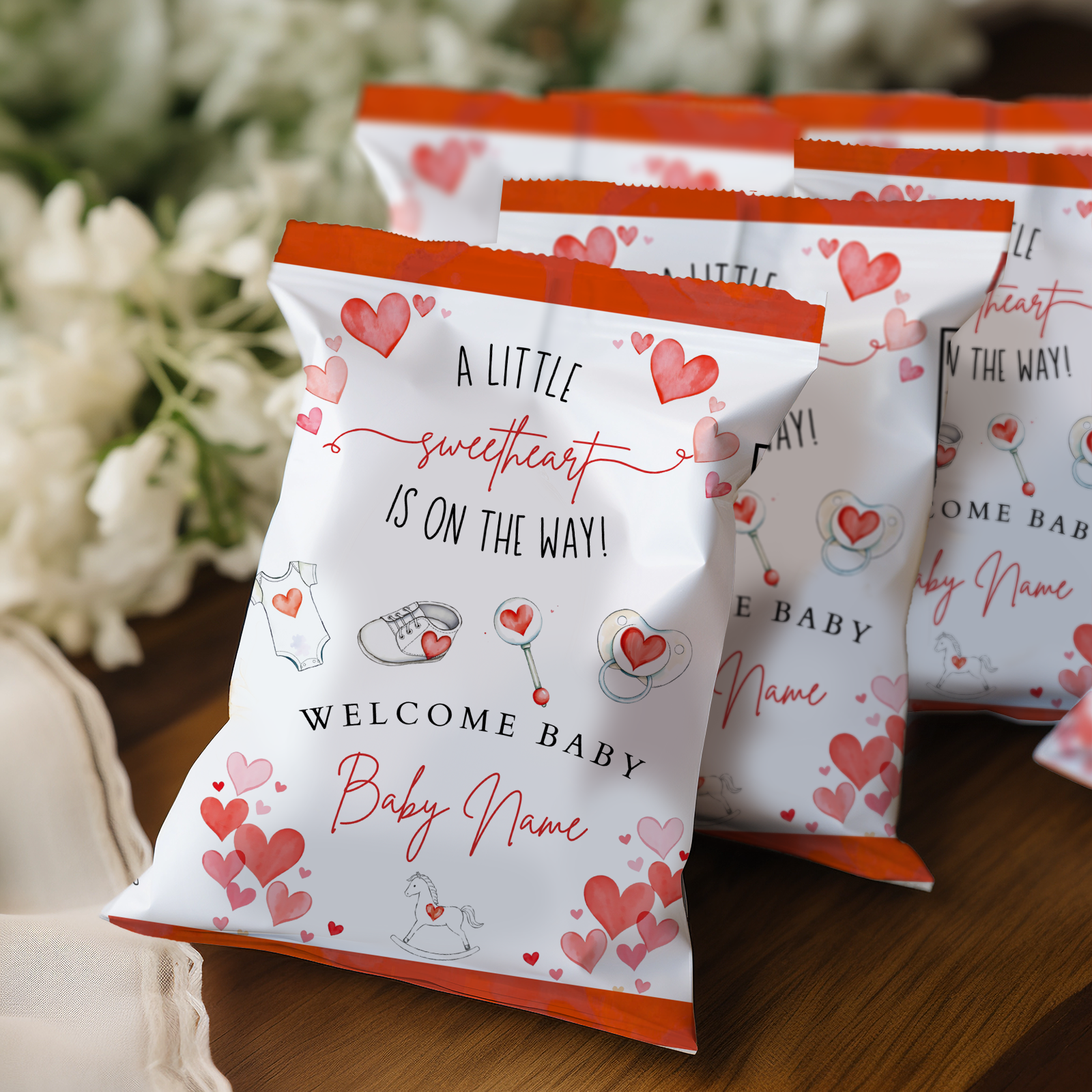Baby shower favor bags with heart designs and text on a wooden surface.
