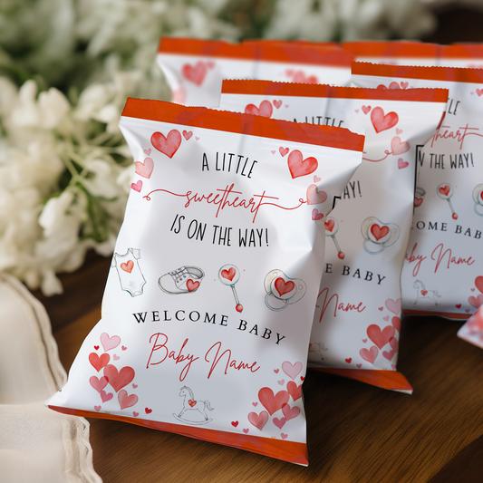 Baby shower favor bags with heart designs and text on a wooden surface.