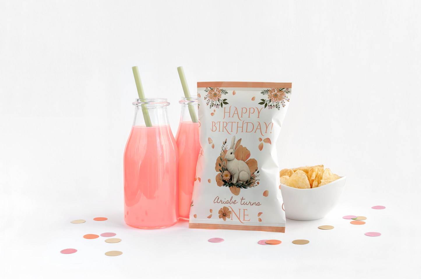 Two bottles of pink juice with straws, a bowl of chips, and a 'Happy Birthday' chip bag on a white background.