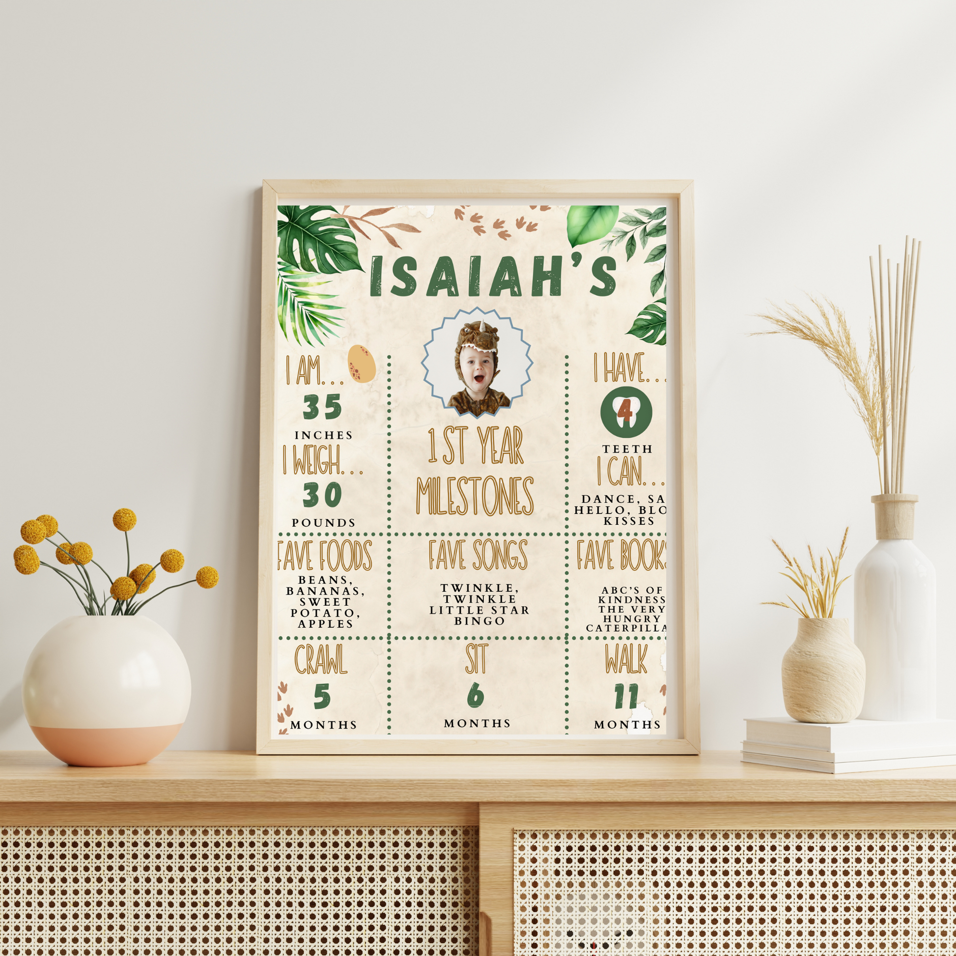 Framed milestone chart for a baby named Isaiah on a decorative shelf with plants.