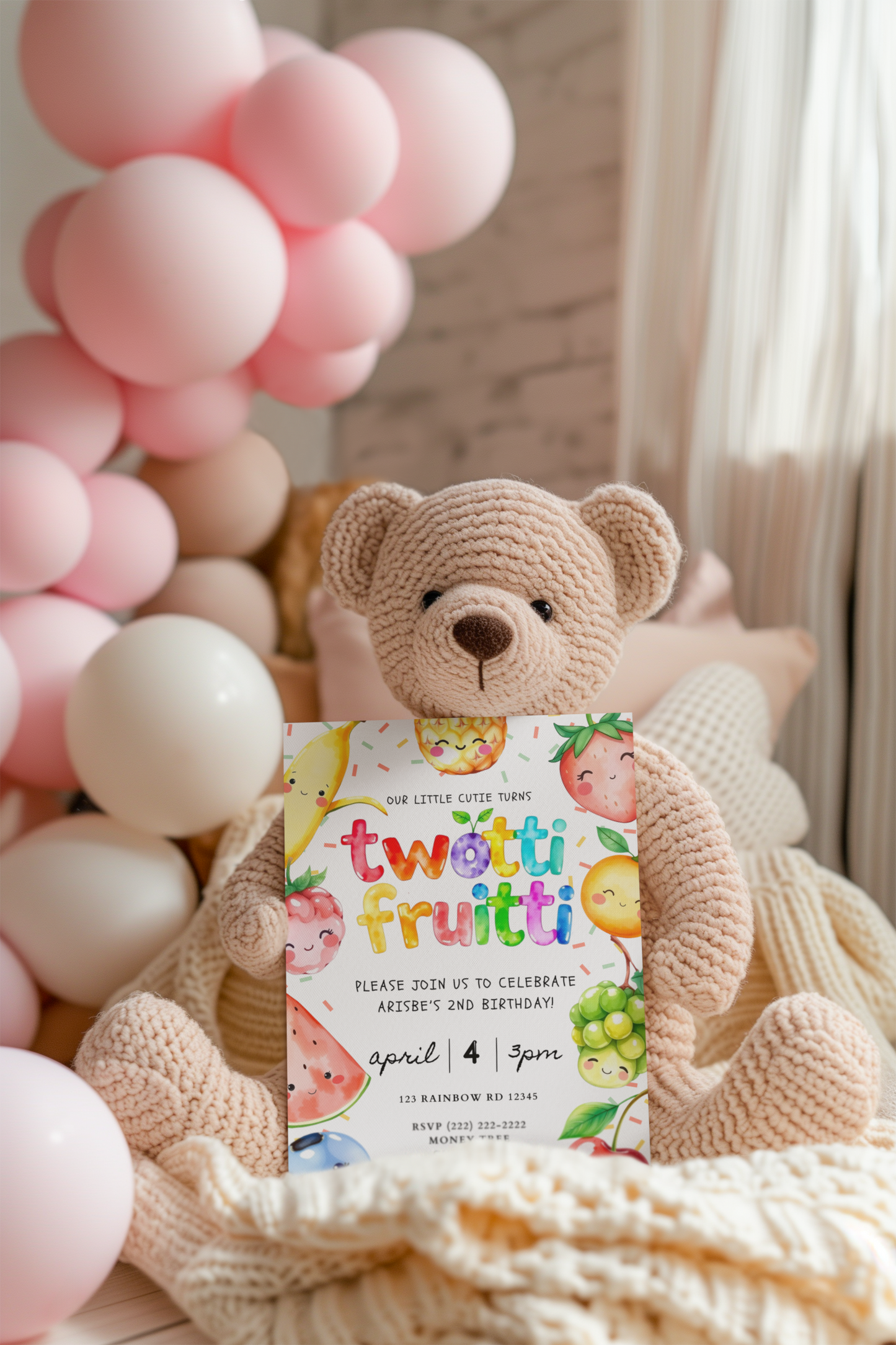 Teddy bear holding a 'twotti fruitti' birthday invitation with pink balloons in the background