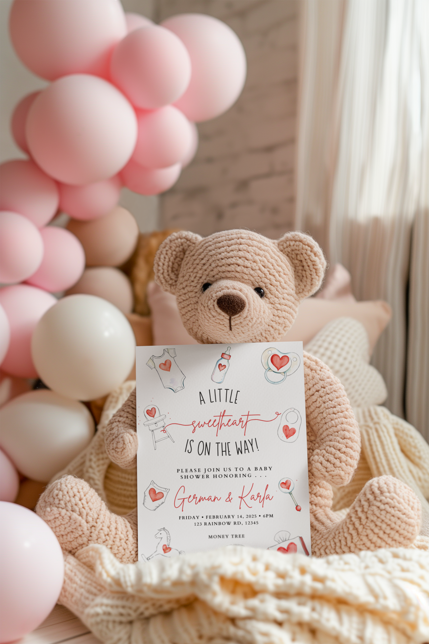 Crocheted teddy bear holding a baby shower invitation with pink balloons in the background.