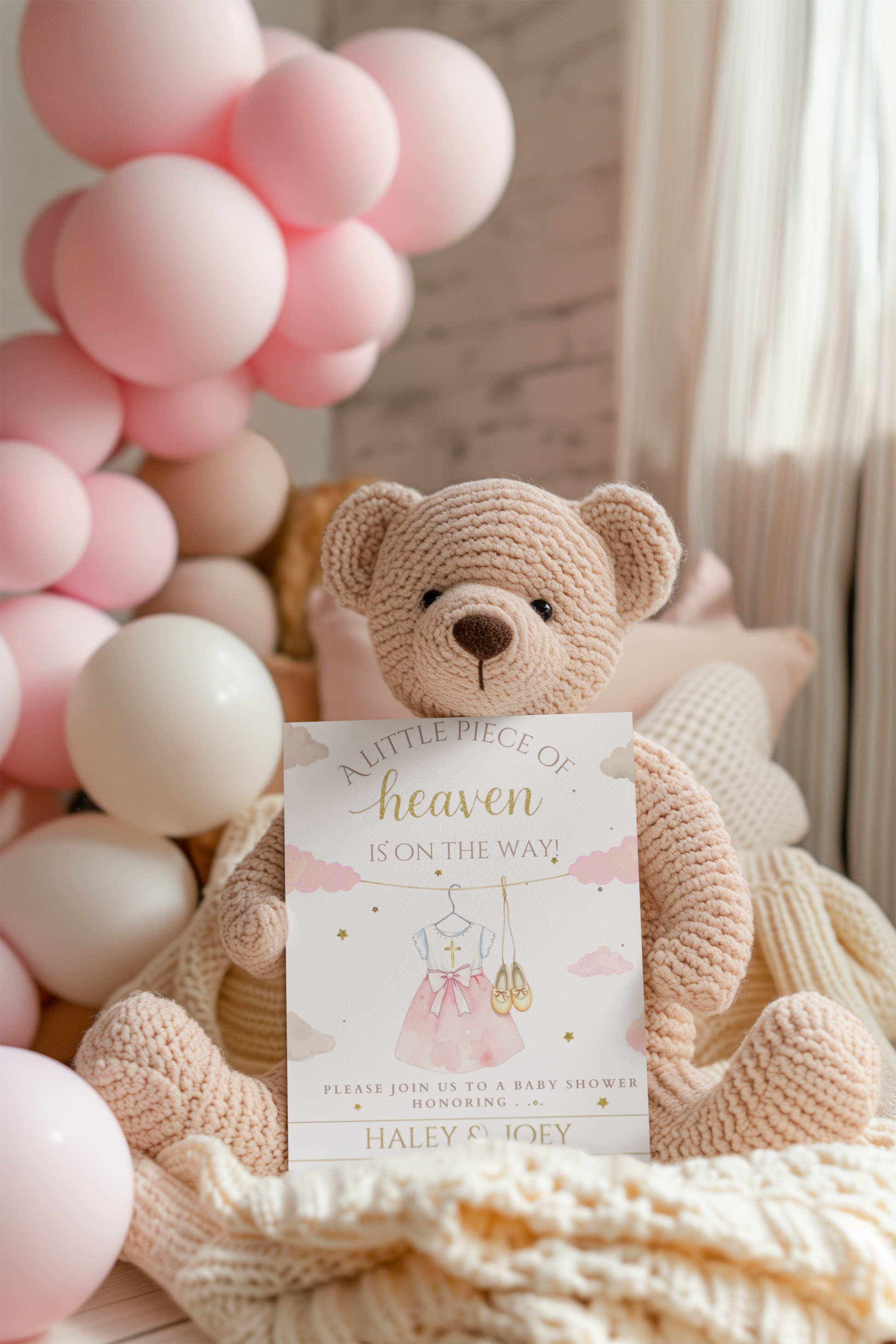 Teddy bear with a baby shower invitation surrounded by pink balloons and a blanket.